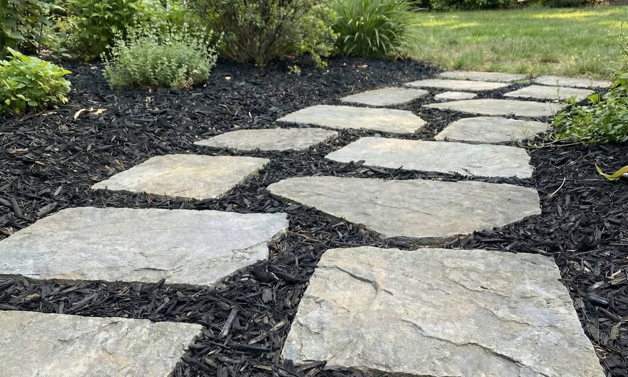 Black mulch securely bonded between live edge pavers with Shabebe Mulch Glue, helping the garden pathway stay neat through everyday foot traffic, pets, wind, and rain.