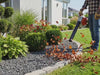 Person using a leaf blower to remove leaves from a flower bed covered with rocks, where rock glue has been applied to keep the stones in place and maintain a tidy surface.